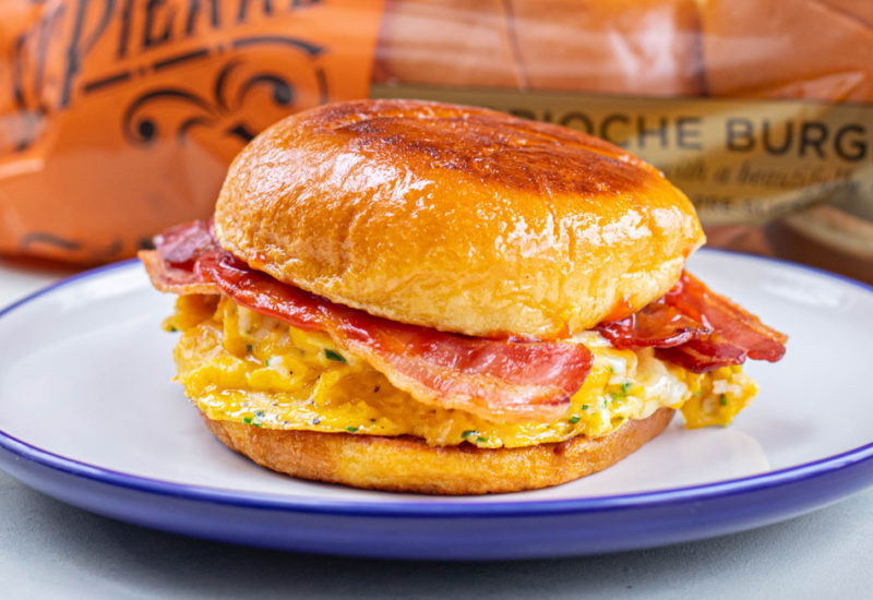 Photo credit: MOB Kitchen A photo of a Brioche French Toast Cheese and Bacon Roll recipe on a white and blue plate with St Pierre Brioche Burger Buns in the background